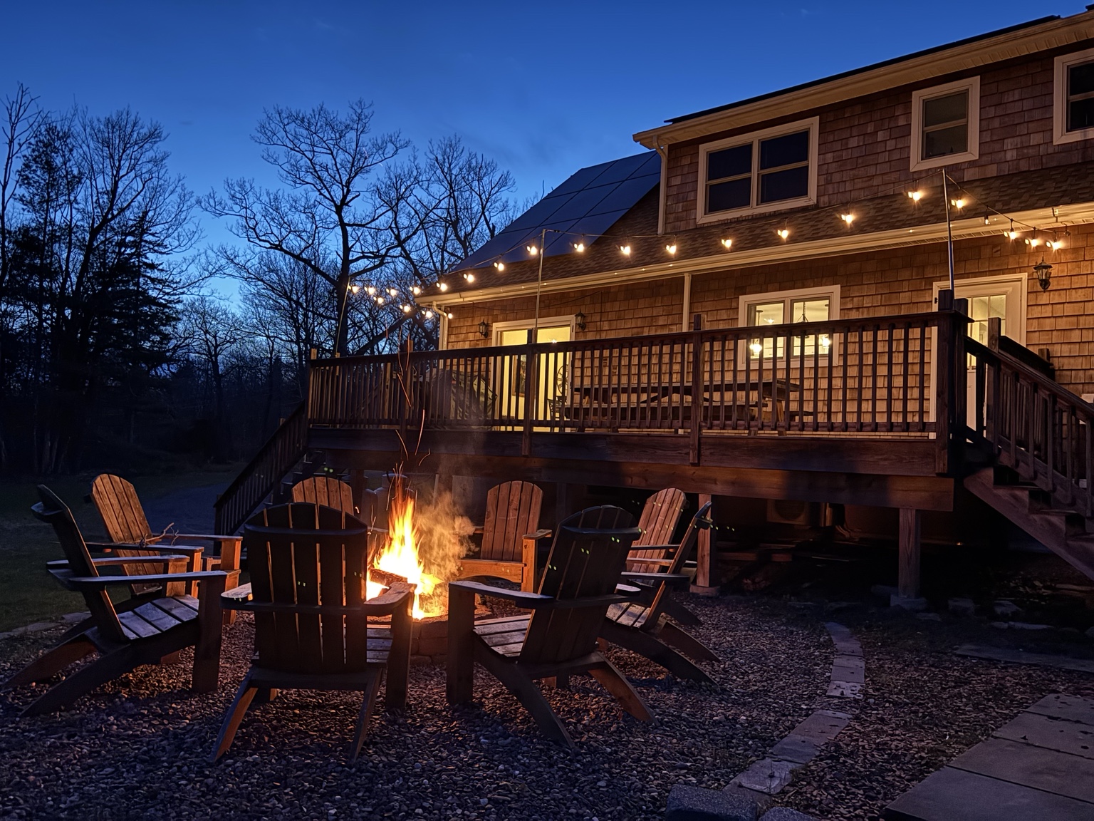 Fire pit glowing beneath string lights behind the Catskills house at dusk