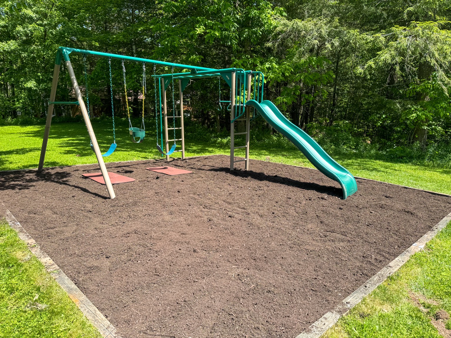 Children's playground with swings, climbing bars, and slide in the private wooded yard